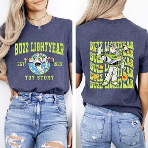 K&ouml;nnte beinhalten: Zwei Frauen tragen marineblaue T-Shirts mit einem gr&uuml;n-wei&szlig;en Buzz Lightyear-Motiv. Das vordere Shirt sagt "Buzz Lightyear Est. 1995 Toy Story" und das hintere Shirt hat ein sich wiederholendes Muster von "Buzz Lightyear".