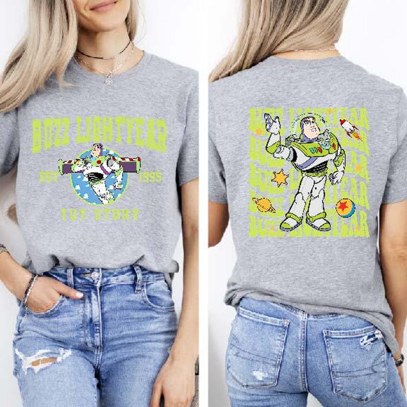 K&ouml;nnte beinhalten: Ein graues T-Shirt mit einer gr&uuml;n-blauen Comicfigur auf der R&uuml;ckseite. Die Figur ist Buzz Lightyear aus der Toy Story-Filmreihe. Die Vorderseite des Shirts zeigt eine Grafik von Buzz Lightyear mit dem aufgedruckten Text "Buzz Lightyear" und "Toy Story".