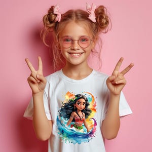 Peut inclure: Un t-shirt blanc avec un imprim&eacute; graphique color&eacute; d'un personnage de dessin anim&eacute; aux longs cheveux noirs, portant un haut rouge et orange et une jupe verte. Le personnage se tient dans une vague bleue et verte.