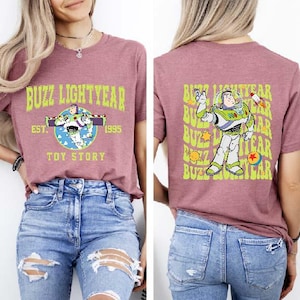 K&ouml;nnte beinhalten: Ein mauvefarbenes T-Shirt mit einem Grafikdruck von Buzz Lightyear aus Toy Story. Die Vorderseite des Shirts zeigt den Schriftzug "Buzz Lightyear Est. 1995 Toy Story". Die R&uuml;ckseite des Shirts hat einen wiederholten Grafikdruck von Buzz Lightyear.