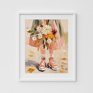 May include: A framed art print of a person holding a bouquet of flowers. The person is wearing a pink dress, green jacket, orange sneakers, and patterned socks. The artwork has a soft, painterly style with autumn leaves scattered on the ground.