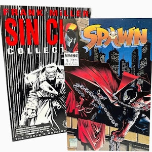 May include: Two comic books are displayed. One is a black and white "Sin City" collection by Frank Miller. The other is a "Spawn" comic book with a cityscape background and a character in a red cape.