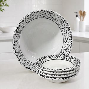 May include: A large white serving bowl and a stack of three smaller matching bowls, all featuring a black speckled pattern along the wide rims and a thin black circular line accenting the interior transition between the rim and the center basin.