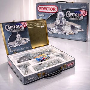 Puede incluir: Un juego Erector de edición limitada con el Capitolio. El juego se presenta en una caja metálica gris con detalles dorados e incluye instrucciones detalladas. La caja muestra un modelo del Capitolio y la bandera estadounidense.