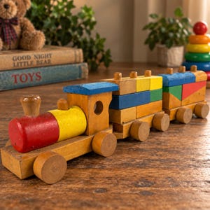 Könnte beinhalten: Ein hölzerner Spielzeugeisenbahnzug bestehend aus einer Lokomotive und zwei verbundenen Wagen. Die Lokomotive hat eine rote zylindrische Front, einen gelben Kessel und ein blaues Dach. Die Wagen bestehen aus gestapelten gelben, blauen und grünen Blöcken.