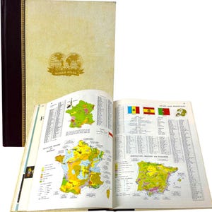 May include: A vintage World Atlas with a beige cover and gold embossed globe design. The open book displays colorful maps of France and Spain, with flags and text. The spine is dark brown with gold accents.