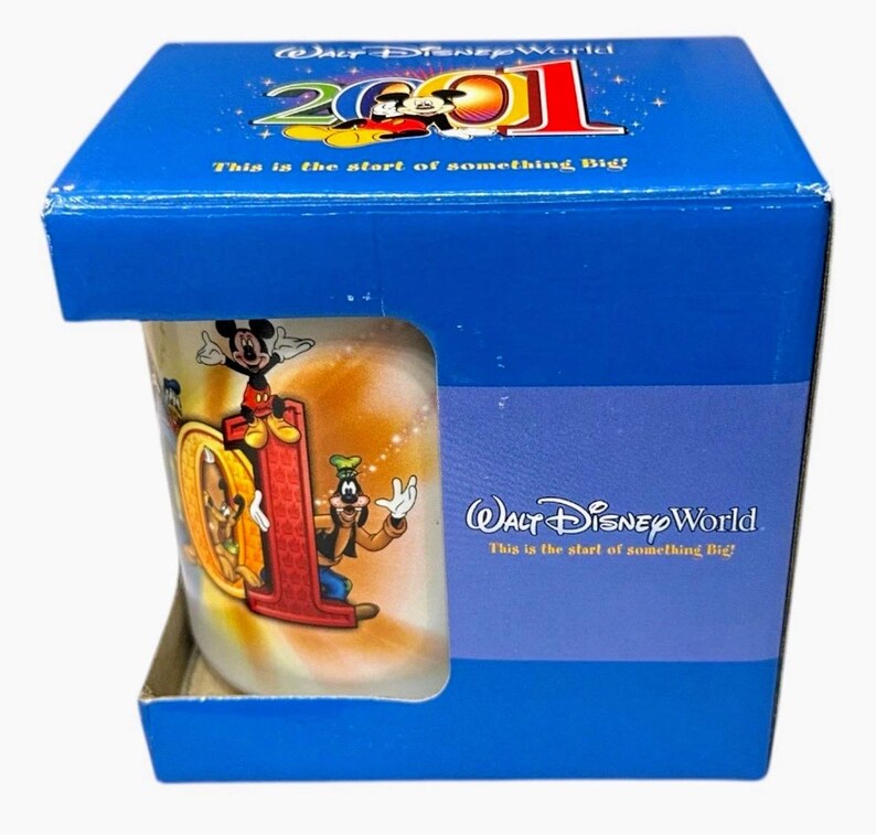 May include: A Walt Disney World 2001 mug in a blue box. The mug features Mickey Mouse, Goofy, and the number "01" in a red color. The box has the text "This is the start of something Big!"