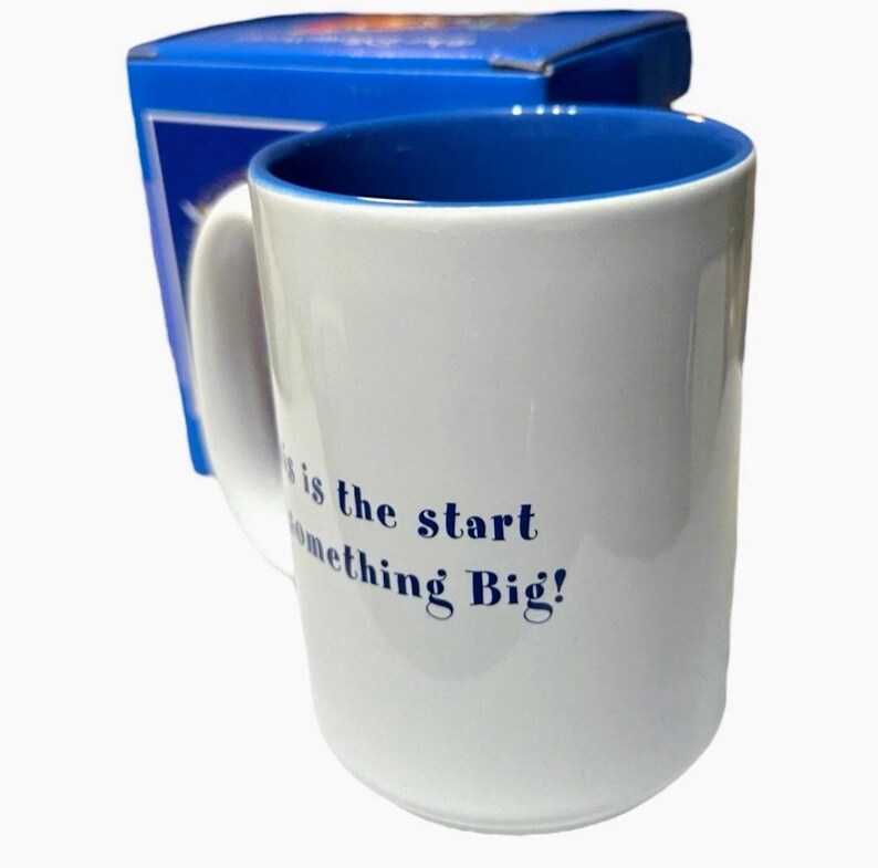 May include: White ceramic mug with a blue interior and handle, accompanied by a blue box. The mug features the text "This is the start of something Big!" in blue lettering. Ideal for coffee, tea, or any beverage.