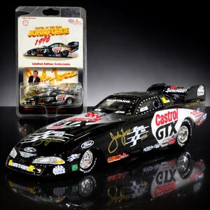 May include: A black and white John Force 1996 Castrol GTX drag racing car model. The model is in a clear plastic case with the words "Driver of the Year" and "Limited Edition Collectible". The car has the Ford logo and the number 34.