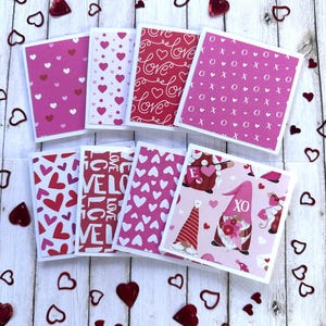 May include: A collection of Valentine's Day cards with various designs, including hearts, the word "love", and gnome illustrations. The cards are in shades of pink and red, scattered with heart-shaped confetti.
