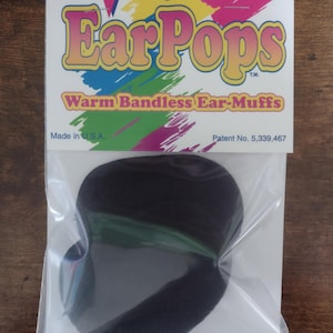 Pode incluir: Um par de protetores de ouvido pretos com uma faixa verde. A embalagem diz "EarPops Warm Bandless Ear-Muffs" e "Made in U.S.A." e "Patent No. 5,339,467".