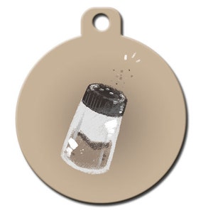 May include: A round, tan-coloured metal tag with a black and white illustration of a salt shaker with salt pouring out of the top.