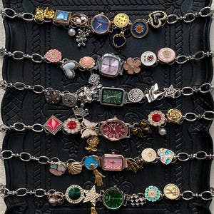 May include: Several decorative watch bracelets with diverse charms. Each bracelet has a silver chain and is decorated with unique charms, including flowers, hearts, and gemstones. The watch faces are in different shapes and colours, adding to the eclectic design.