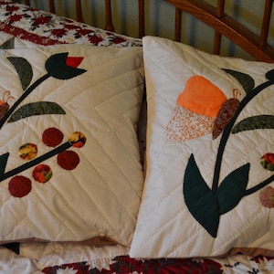 May include: Two white pillowcases with embroidered floral designs. The designs feature butterflies, leaves and berries in shades of green, orange and red.