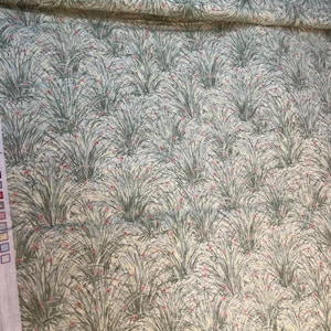 May include: Fabric with a repeating pattern of stylized green grass and small red flowers on a light cream background. The fabric has a soft, muted color palette, with a subtle texture. The design is reminiscent of a meadow or field.