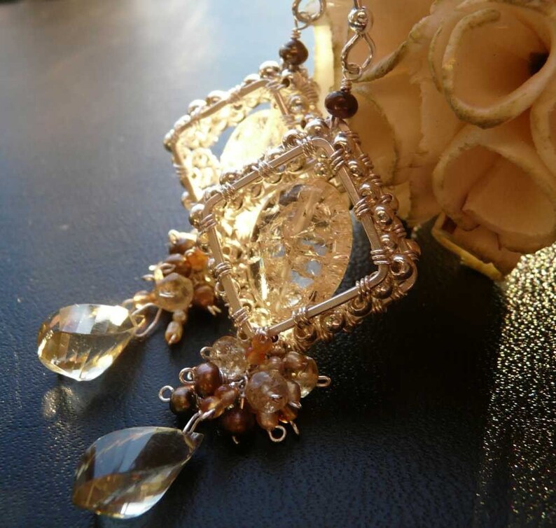May include: Silver wire earrings with a clear crystal cage and brown and clear gemstone accents.