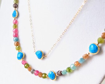Puede incluir: Un collar de dos capas con una cadena de oro y cuentas de piedras preciosas de colores. Las cuentas son una mezcla de rosa, verde, azul y marrón. El collar presenta detalles turquesa.