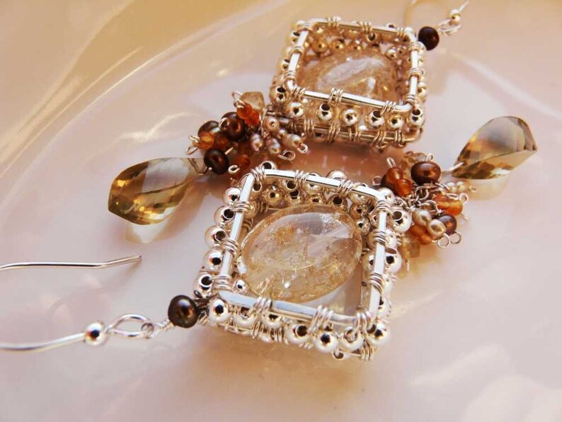 May include: A pair of silver wire wrapped earrings with clear quartz stones and brown and gold beads.
