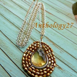 May include: A gold and silver chain necklace with a teardrop-shaped yellow gemstone pendant surrounded by gold beads.