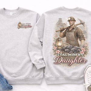 May include: Light gray sweatshirt with the text "COAL MINER'S DAUGHTER" and a graphic of a coal miner. The back of the sweatshirt features a detailed illustration of a miner with a pickaxe, a lantern, and coal.