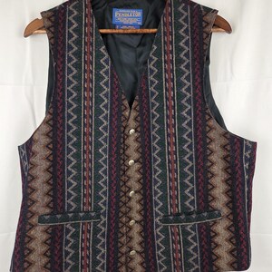 May include: A Pendleton vest featuring a multi-colored geometric pattern in shades of dark blue, forest green, burgundy, and tan. The vest has a V-neckline, five silver-toned metal buttons down the front, and two horizontal welt pockets.