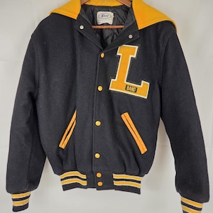 May include: A black varsity jacket with a yellow hood, yellow snap buttons, and yellow striped cuffs and hem. A large yellow letter L with the word BAND is appliqued on the left chest. The jacket features a quilted black lining and a white inner label.