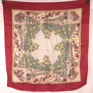 May include: A square scarf with a deep red border and a central cream-colored panel featuring a detailed illustration of a tree-lined park with figures in historical attire. The design includes four corner vignettes of buildings and the Liberty logo.