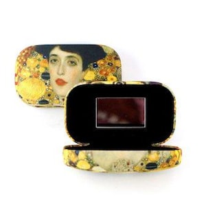 May include: A small, rectangular box with a hinged lid. The lid is decorated with a painting of a woman with a gold background. The inside of the box is lined with black velvet.