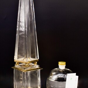May include: A clear glass bottle with a gold lid and a label that reads "Pinnacle" sits on a black surface next to a tall, clear glass obelisk with a gold base.  There are three small, round stones stacked on a small, brown, rectangular stone.