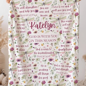 May include: A white blanket with a floral and dragonfly pattern, featuring inspirational text and the name "Katelyn" in a script font. The blanket has purple and pink flowers and green dragonflies.