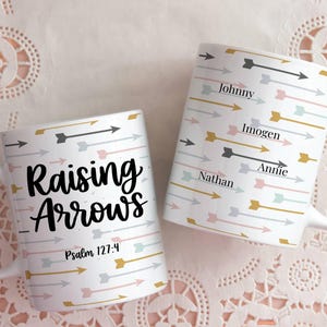 May include: Two white ceramic mugs with arrow patterns in gray, gold, and pink. One mug reads "Raising Arrows" with "Psalm 127:4" below. The other mug has names: Johnny, Imogen, Nathan, and Annie.