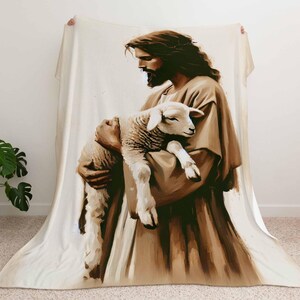 Op de afbeelding: Een bruin en wit fleece deken met een schilderij van een man die een lam vasthoudt. De man draagt een lange robe en heeft een baard. Het lam is wit en heeft een zwarte neus.