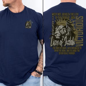 May include: A navy blue t-shirt with a lion graphic on the back. The graphic features a lion with a crown, the text "Lion of Judah", and the Bible verse Revelation 5:5. The text "VICTORIOUS" is written vertically on the right side of the graphic.
