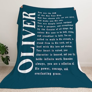 May include: A teal blue fleece blanket with white text that reads "OLIVER You are the SON of the One True King God has chosen you, set you apart and made you His own. You are deeply loved, equipped with a purpose, and strengthened by the Creator of all things. God raises His sons to be bold, strong and steadfast in faith. You are called to walk in His strength, to stand firm in His truth, and to lead with His love and wisdom. Your heart is valued, your character is honored, and your life holds infinite worth. Remember always, you are a reflection of His power, courage, and everlasting grace."