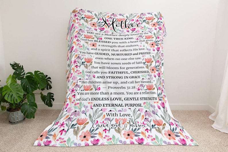 May include: A floral-patterned blanket with a white background and pink, purple, and orange flowers. The blanket has text that reads "Mother" and a loving message. The blanket is a thoughtful gift.