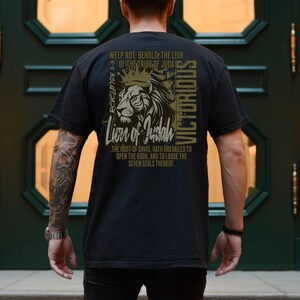 May include: Black t-shirt featuring a lion graphic and the text "Weep not: Behold, the Lion of the Tribe of Juda Revelation 5:5 Lion of Judah The root-of David, hath prevailed to open the book, and to loose the seven seals thereof. Victorious"