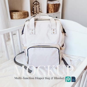 Op de afbeelding: Een lichtbeige multifunctionele luiertas met een voorvak en een donkerblauwe rand. De tas heeft een handvat aan de bovenkant en een schouderriem. De tekst "MOCKUP" en "Multi-function Diaper Bag & Blanket" zijn zichtbaar.