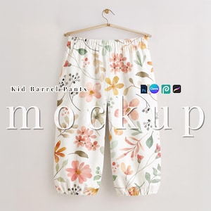 Op de afbeelding: Witte kinderbarrelbroek met een bloemenpatroon in roze, oranje en gele tinten. De broek hangt aan een houten hanger tegen een witte achtergrond. De tekst "Kid Barrel Pants" is zichtbaar.