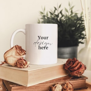 May include: White ceramic mug with a black inscription that reads "Your design here" on a stack of books with dried roses.