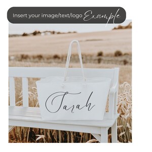 May include: White tote bag with the name "Sarah" written in cursive on the front. The bag is sitting on a white bench in a field.