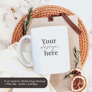 May include: White ceramic mug mockup with the text "Your design here" on a beige fabric background with a wicker coaster and dried fruit.