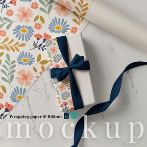 May include: A white gift box with a navy blue ribbon and bow, decorated with floral wrapping paper. The wrapping paper features a pattern of blue, peach, and yellow flowers with green leaves on a white background. The words "Wrapping paper & Ribbon mockup" are visible.
