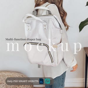 Op de afbeelding: Een witte luiertas met zwarte en gouden accenten. De tas wordt gedragen door een persoon en heeft de tekst "Multi-function diaper bag" en "mockup" erop.