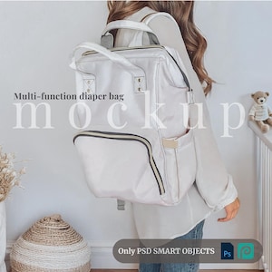 Op de afbeelding: Een witte luiertas met gouden accenten en meerdere vakken. De tas wordt door een persoon gedragen. De tekst "Multi-function diaper bag mockup" is zichtbaar in de afbeelding.