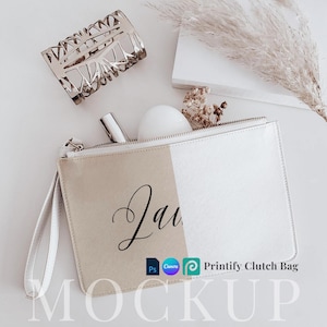 May include: A white and beige clutch bag with a zip fastening and a white strap. The bag has the word "Laura" written in black cursive on the front. The bag is lying on a white surface with a white book and a gold bracelet.