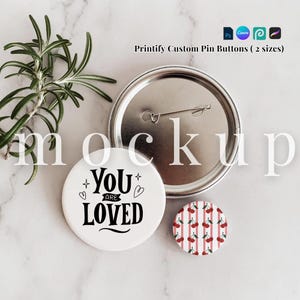 May include: Two circular pin buttons and one metal pin back component. One button is white with black text reading YOU ARE LOVED and small heart and star icons. The other button features a red and white vertical striped pattern with red cherries.