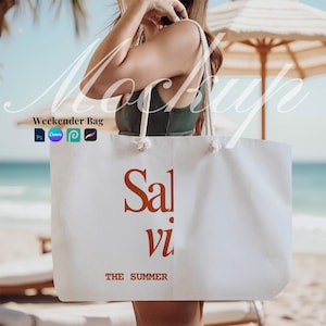 May include: A white canvas weekender bag with rope handles. The bag features the text "Salvi" in a burnt orange color, with "THE SUMMER" printed below. The bag is held in front of a beach scene.