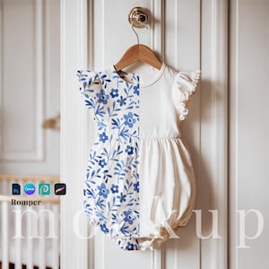May include: A white baby romper with blue floral print on one side. The romper has a ruffled neckline and short sleeves.