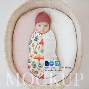 May include: A baby swaddled in a white and cream swaddle with a mushroom and leaf pattern. The baby is wearing a red beanie and is lying in a wicker basket. The text "Baby Set - Crib sheet, Swaddle, Beanie" is visible below the baby.