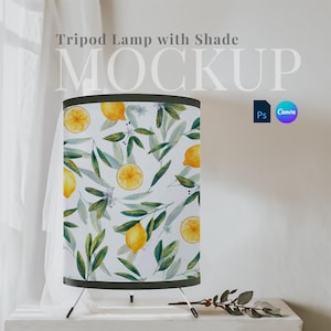 May include: Tripod lamp with a white shade featuring a lemon and leaf pattern. The lamp is on a white surface with a small branch.